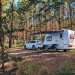 A caravan parked in a forested area with a car beside it