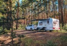 A caravan parked in a forested area with a car beside it