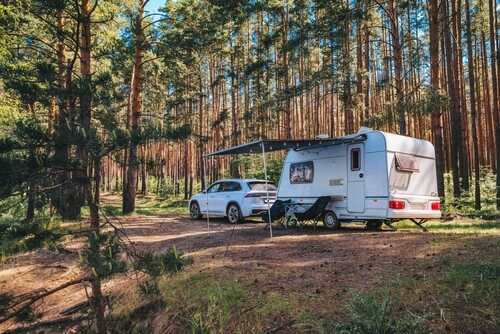 A caravan parked in a forested area with a car beside it