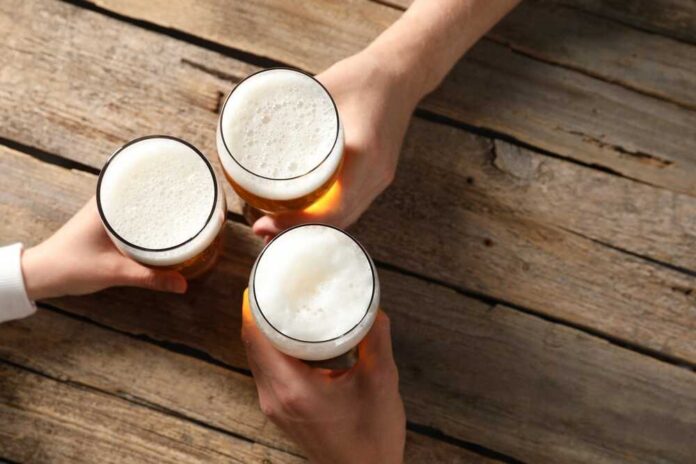 Friends,With,Glasses,Of,Beer,At,Wooden,Table,,Top,View. Three hands holding beer glasses in a toast