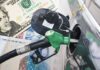 A fuel pump nozzle inserted into a car's gas tank with various currency notes in the background