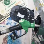 A fuel pump nozzle inserted into a car's gas tank with various currency notes in the background