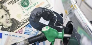 A fuel pump nozzle inserted into a car's gas tank with various currency notes in the background
