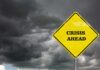 A yellow warning sign that reads 'CRISIS AHEAD' against a backdrop of dark, stormy clouds