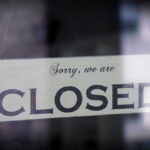 A sign hanging in a window that reads 'Sorry, we are CLOSED'