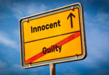 A yellow road sign displaying 'Innocent' pointing up and 'Guilty' crossed out