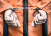 Murderous Affair Ends In Life Prison Sentence Handcuffed person in orange jumpsuit behind prison bars.