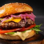 Burger Bloodbath Hits California – CLOSED! Close-up of a gourmet cheeseburger with lettuce, tomato, and pickled onions