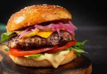 Burger Bloodbath Hits California – CLOSED! Close-up of a gourmet cheeseburger with lettuce, tomato, and pickled onions