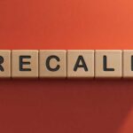 Mystery Specks Trigger Massive Recall Wooden letter tiles spelling recall on an orange background