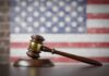 A wooden gavel resting on a sound block with an American flag background