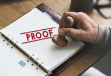 A hand holding a wooden stamp over a document marked 'PROOF'