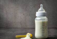 A baby bottle filled with milk next to a scoop of powdered formula