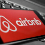Airbnb’s AI Blacklists July 4 Travelers Airbnb logo on a phone screen, near keyboard.