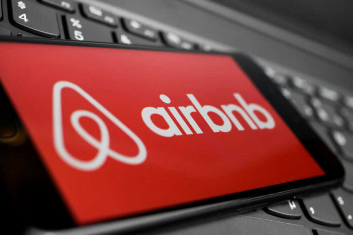 shutterstock_1861555885 Airbnb logo on a phone screen, near keyboard.