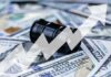Oil Shock Explodes Prices – AGAIN! An oil barrel placed on a background of dollar bills with an upward trend graph overlay