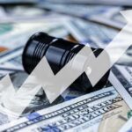 Oil Shock Explodes Prices – AGAIN! An oil barrel placed on a background of dollar bills with an upward trend graph overlay