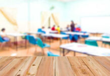 Schools Arm Up With Pepper Drones – DETAILS Blurred classroom with students and a wooden foreground.