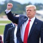 Spy-Movie Swap: Trump Vanishes on Tarmac Donald Trump raising their arm in a fist gesture near a car.