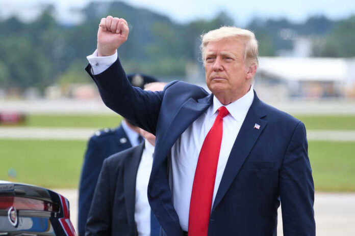 shutterstock_1821865592 Donald Trump raising their arm in a fist gesture near a car.