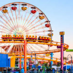 Beloved Park Shuttered — What Killed It? Colorful amusement park scene featuring a ferris wheel and roller coaster at sunset