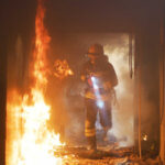 Firefighter with flashlight walking through a burning hallway