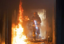 Firefighter with flashlight walking through a burning hallway