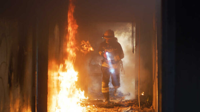 Firefighter with flashlight walking through a burning hallway