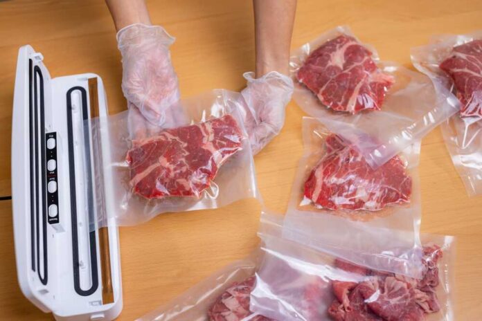 Hands wearing gloves vacuum sealing meat in plastic bags