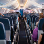 Airlines Tax The Overhead Now Airplane interior with passengers seated mid-flight.