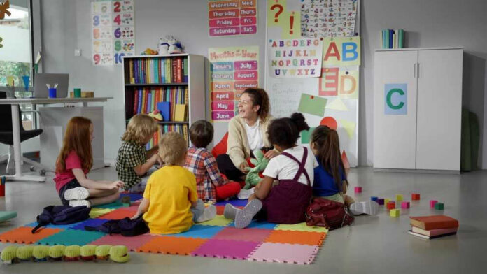 shutterstock_2319071899 Children sitting on the floor around a teacher.