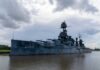 A large battleship docked in calm waters under a cloudy sky