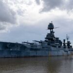 A large battleship docked in calm waters under a cloudy sky