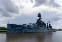 Danube Drops, Warships Rise A large battleship docked in calm waters under a cloudy sky