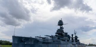 A large battleship docked in calm waters under a cloudy sky