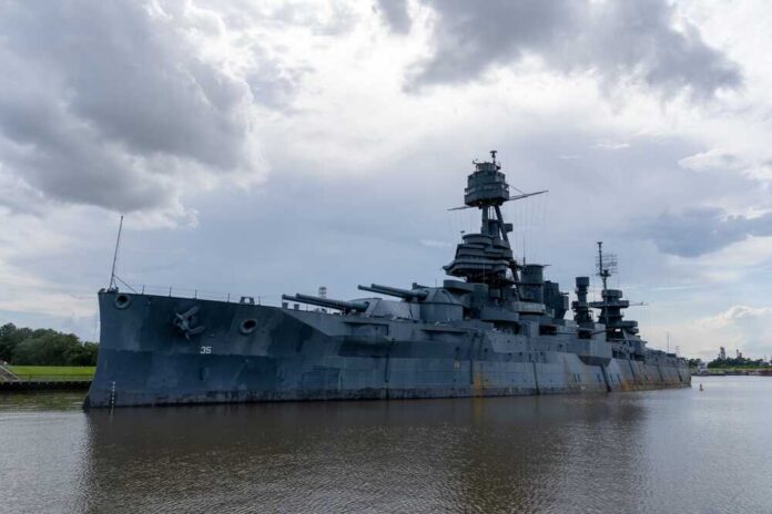 A large battleship docked in calm waters under a cloudy sky