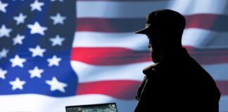Silhouette of a person using a laptop before a large US flag