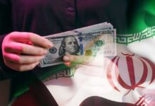 Economic D-Day: Trump Targets Iran’s Wallet A person holding a stack of US hundred-dollar bills in front of the Iranian flag