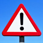 Rescue Mission Hit — Sailors Killed A triangular warning sign with an exclamation mark against a blue sky