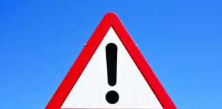 A triangular warning sign with an exclamation mark against a blue sky