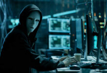 Iranian Hackers Twist America’s Valves Person in hoodie and mask using computer, multiple screens.