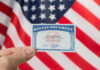 Hand holding social security card, American flag background.
