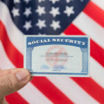 Retire at 60? Congress Floats Shock Move Hand holding social security card, American flag background.