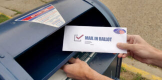 Hands mailing a ballot envelope into a blue mailbox