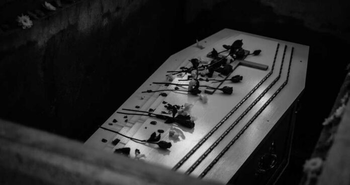 Coffin with flowers inside a dark burial plot.
