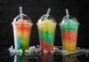 Three colorful shaved ice drinks in clear plastic cups with domed lids