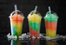 Three colorful shaved ice drinks in clear plastic cups with domed lids