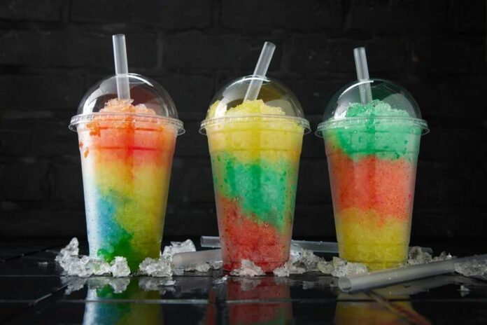 Assortment,Of,Various,Slush,Drinks,In,A,Row,On,Black Three colorful shaved ice drinks in clear plastic cups with domed lids
