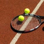 Wimbledon Shock: Tennis Icon’s Health Battle Revealed Tennis racket and balls on a clay court near a white line