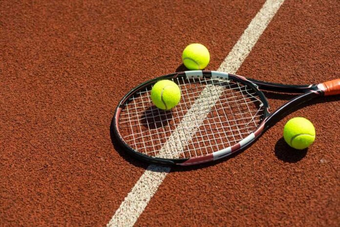 Tennis,Racket,With,A,Tennis,Ball,On,A,Tennis,Court Tennis racket and balls on a clay court near a white line